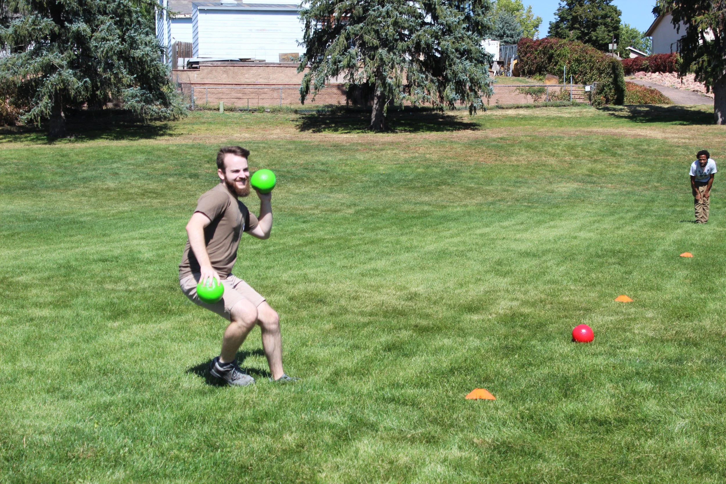 Two people playing bocce ball on a grassy lawn with trees in the background.