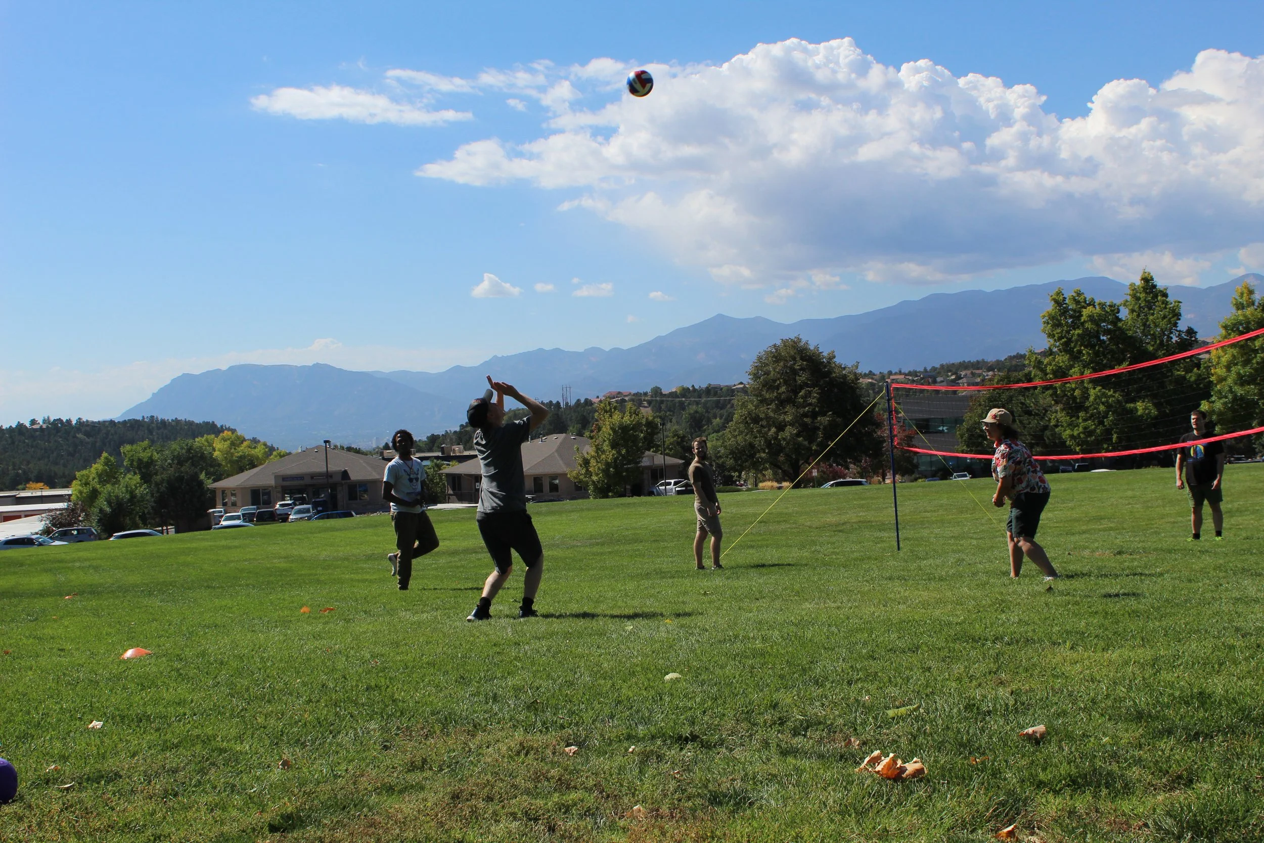 People playing volleyball on a grass field with mountains in the background