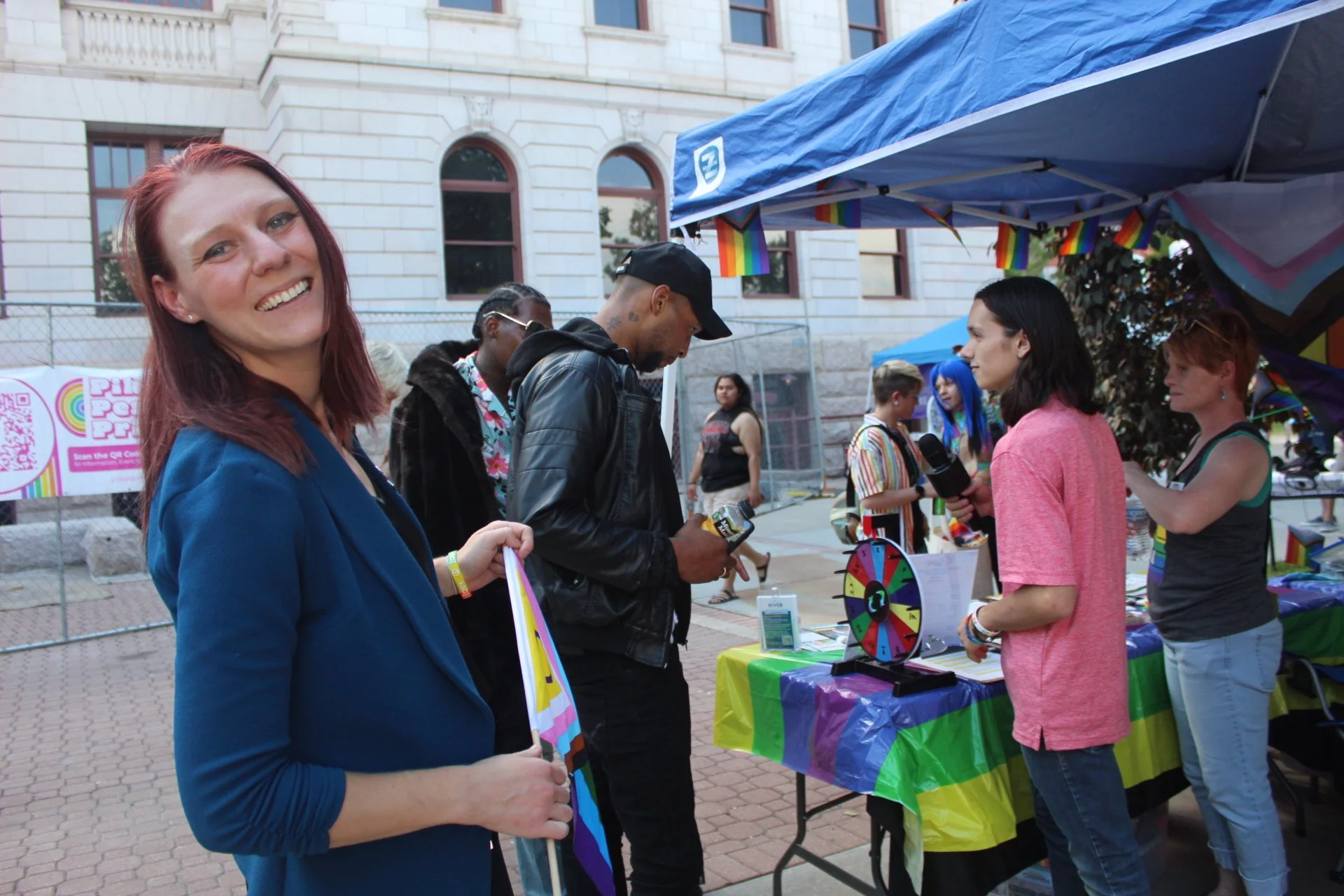 Outdoor event with people near a booth with rainbow flags and decorations.