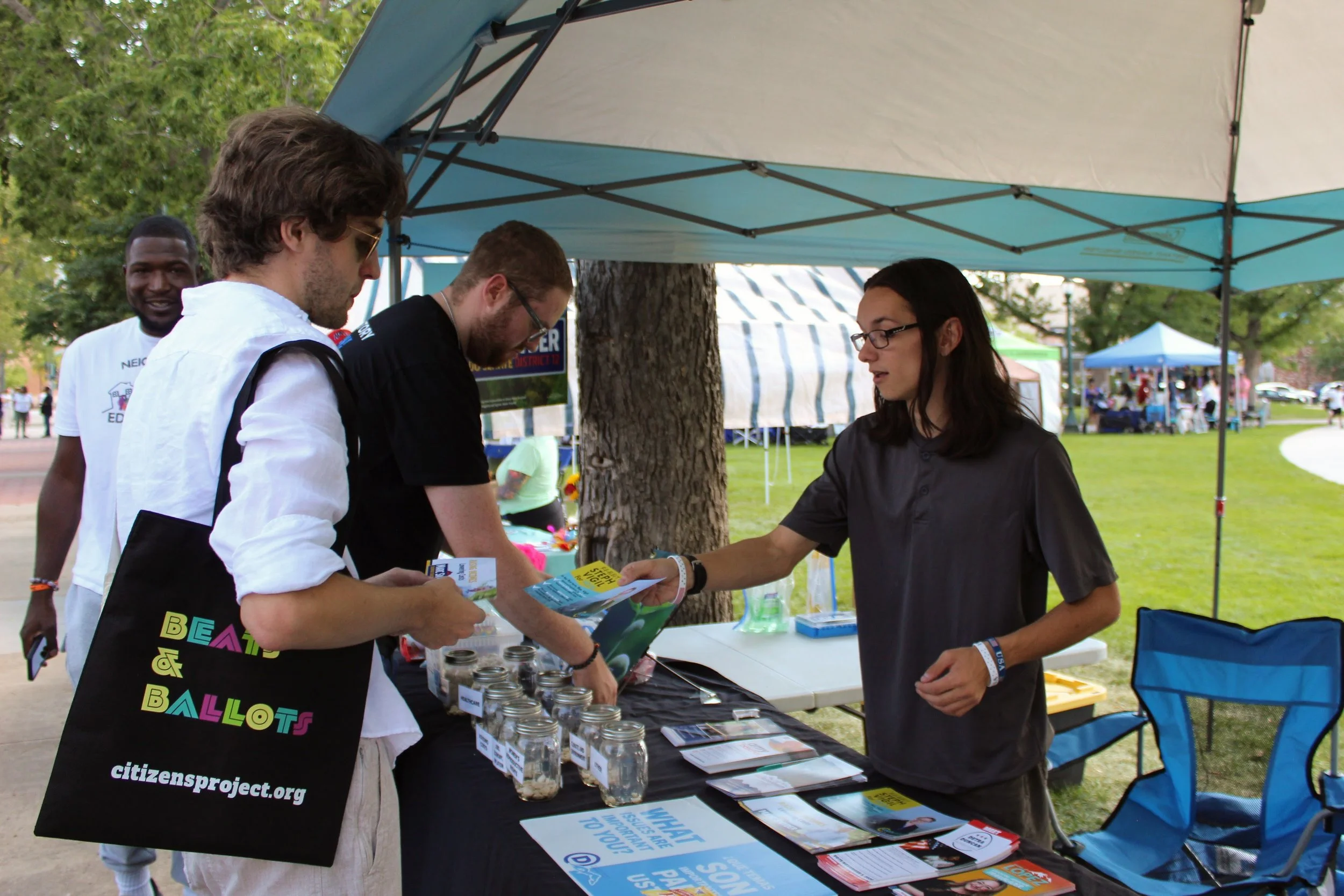 People interacting at an outdoor booth with informational brochures and jars.