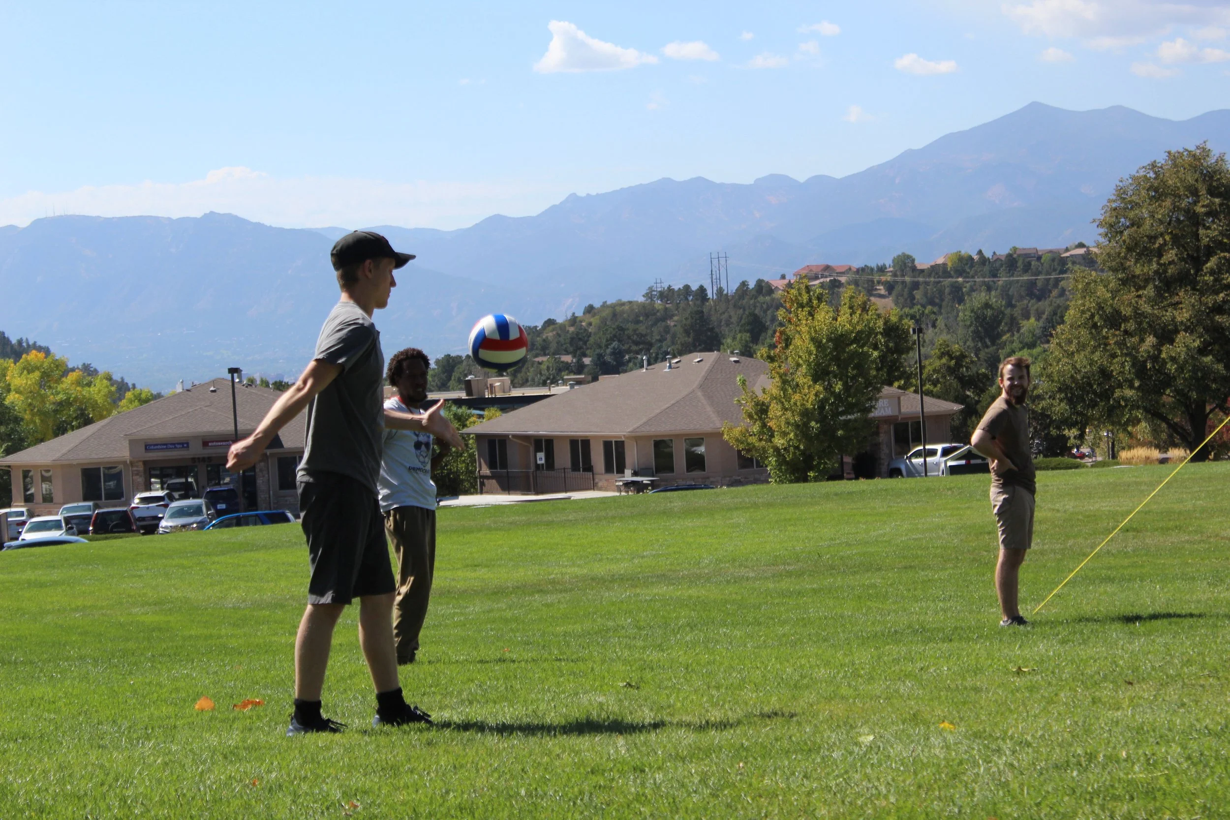 Group playing volleyball on a grassy field with mountains in the background.