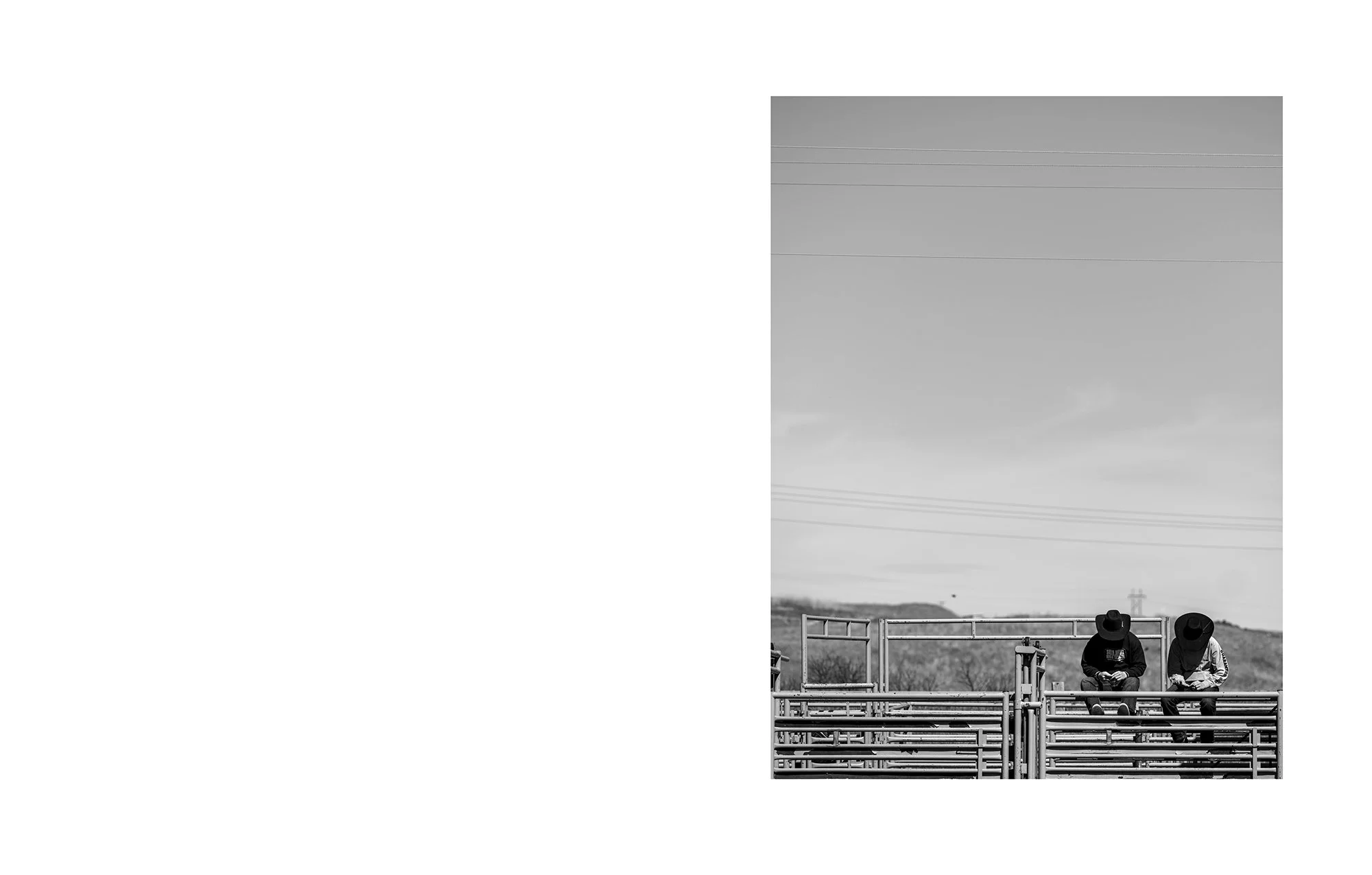 Two individuals sitting on bleachers outdoors, wearing hats and looking at their phones, with power lines and open landscape in the background.