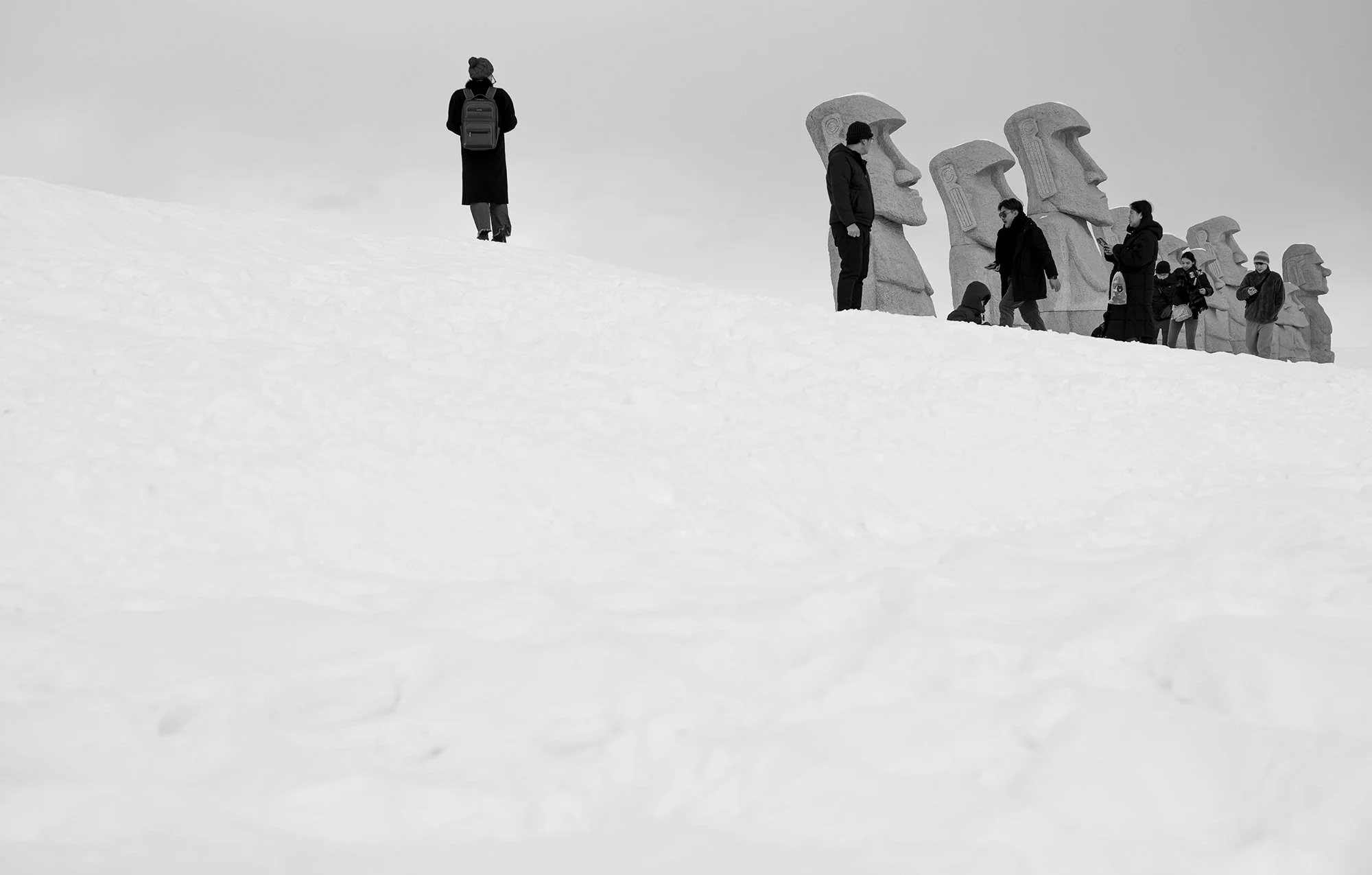 People standing near giant carved stone statues on snow-covered ground, with one person walking away from the group.
