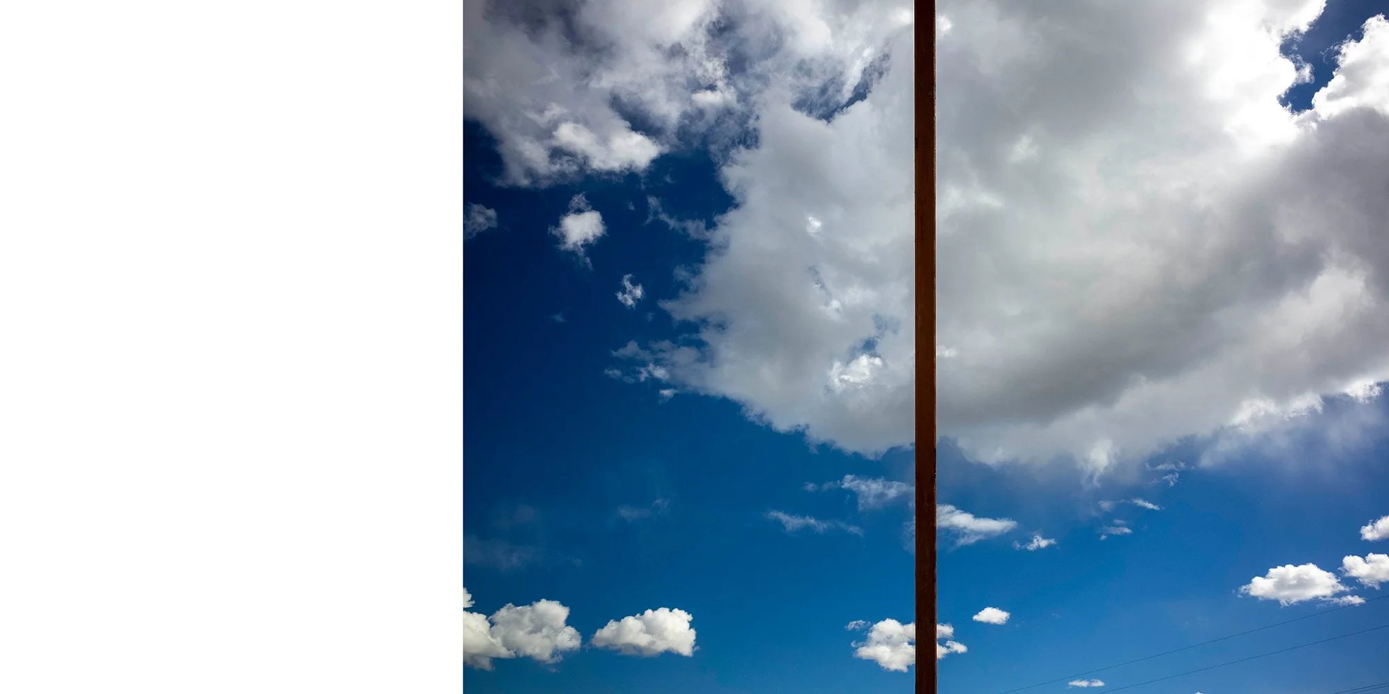 Sky filled with white and gray clouds, with a vertical brown pole in the middle.