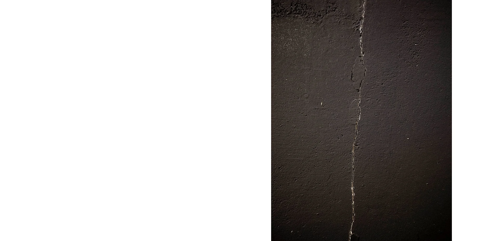 Close-up of a dark, textured concrete wall with a vertical crack running through it.
