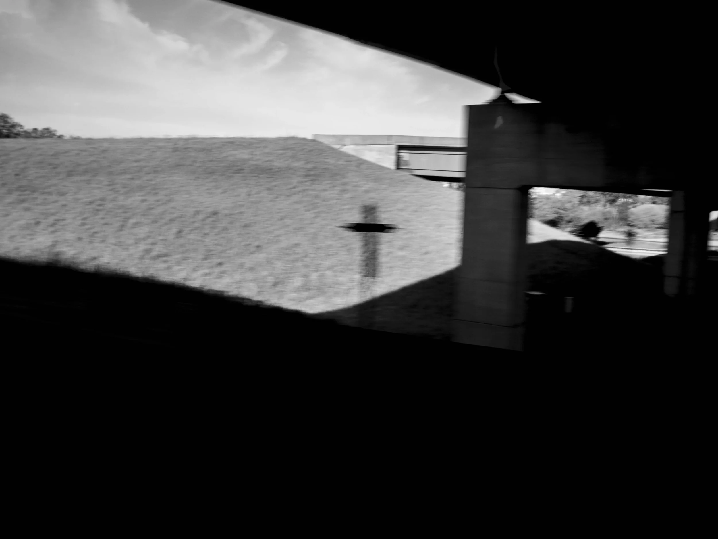 Black-and-white photo of a grassy landscape seen through a window or opening, with a bridge or overpass in the background.