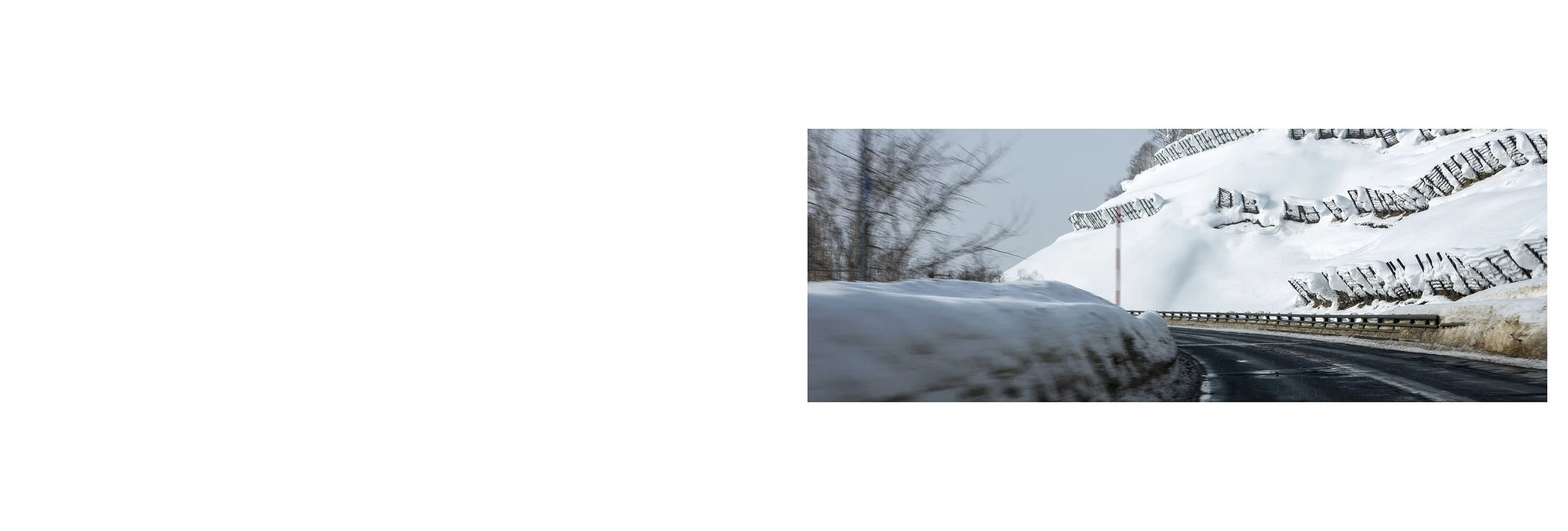 Snow-covered mountain road with snowbanks and snow sliding down rock formations, winter landscape.