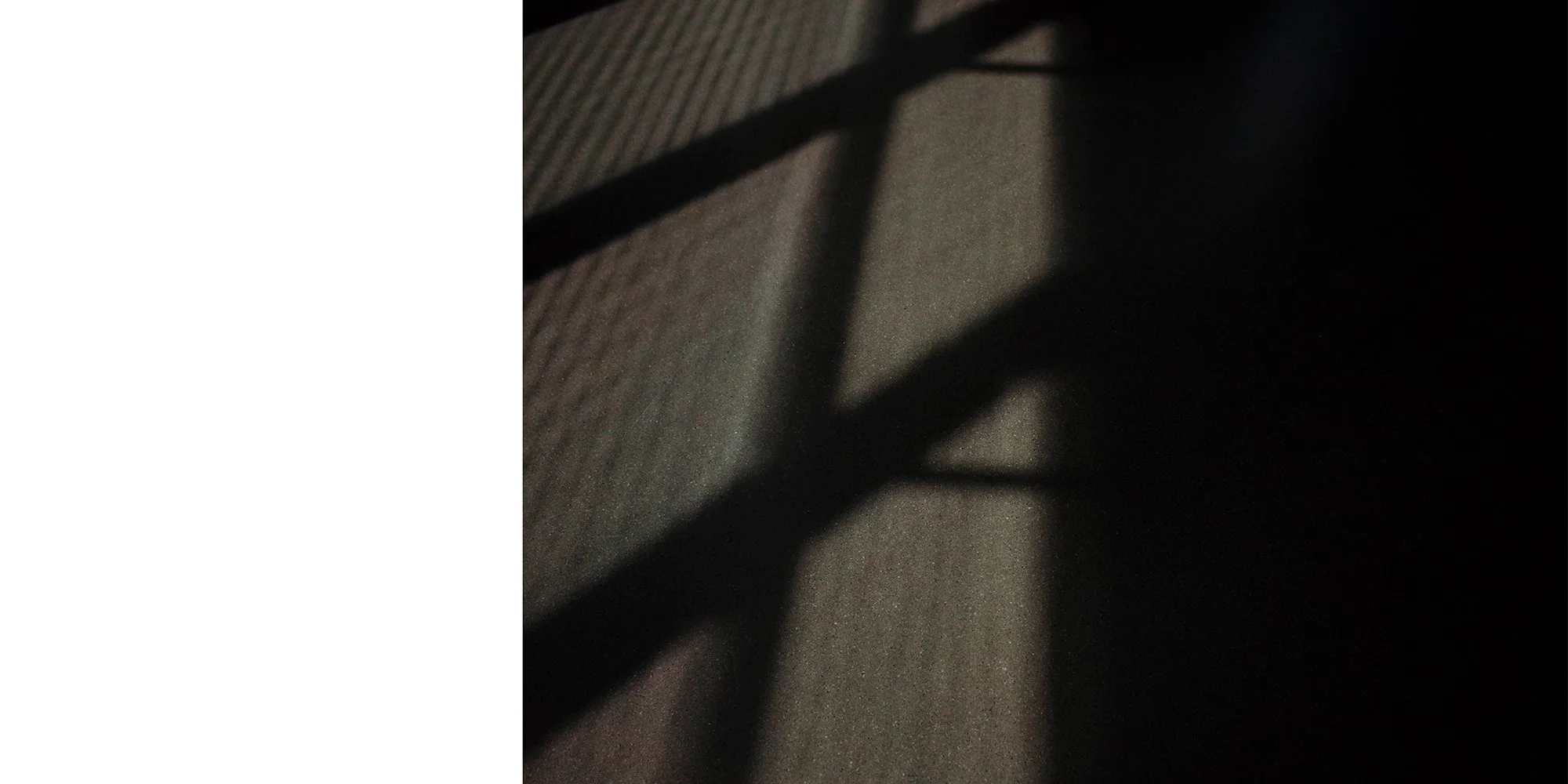 Shadows of bars or railings cast on a textured surface, possibly a carpet or fabric, with light creating contrast in the scene.