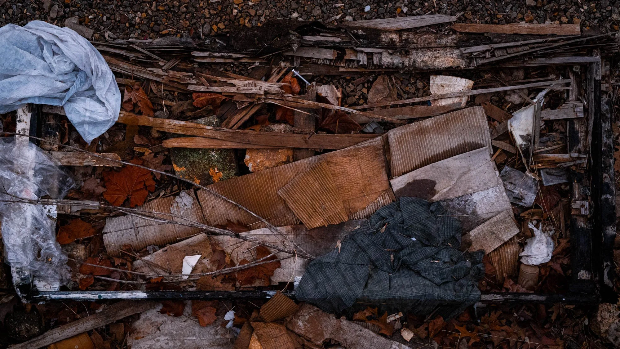 Debris and trash including fabric, wood, leaves, and plastic scattered in a small, cluttered area.