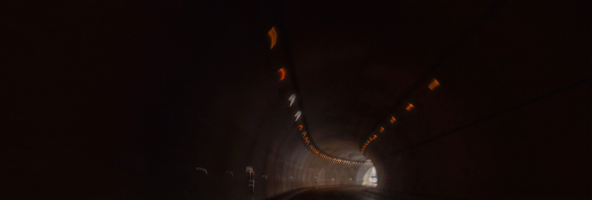 A dark tunnel with orange and white lights along the ceiling, appearing blurry due to motion.