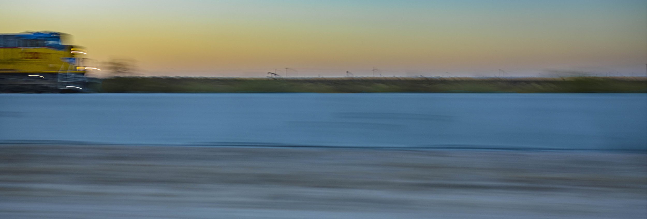 A blurred moving yellow semi-truck driving on a highway at sunset.