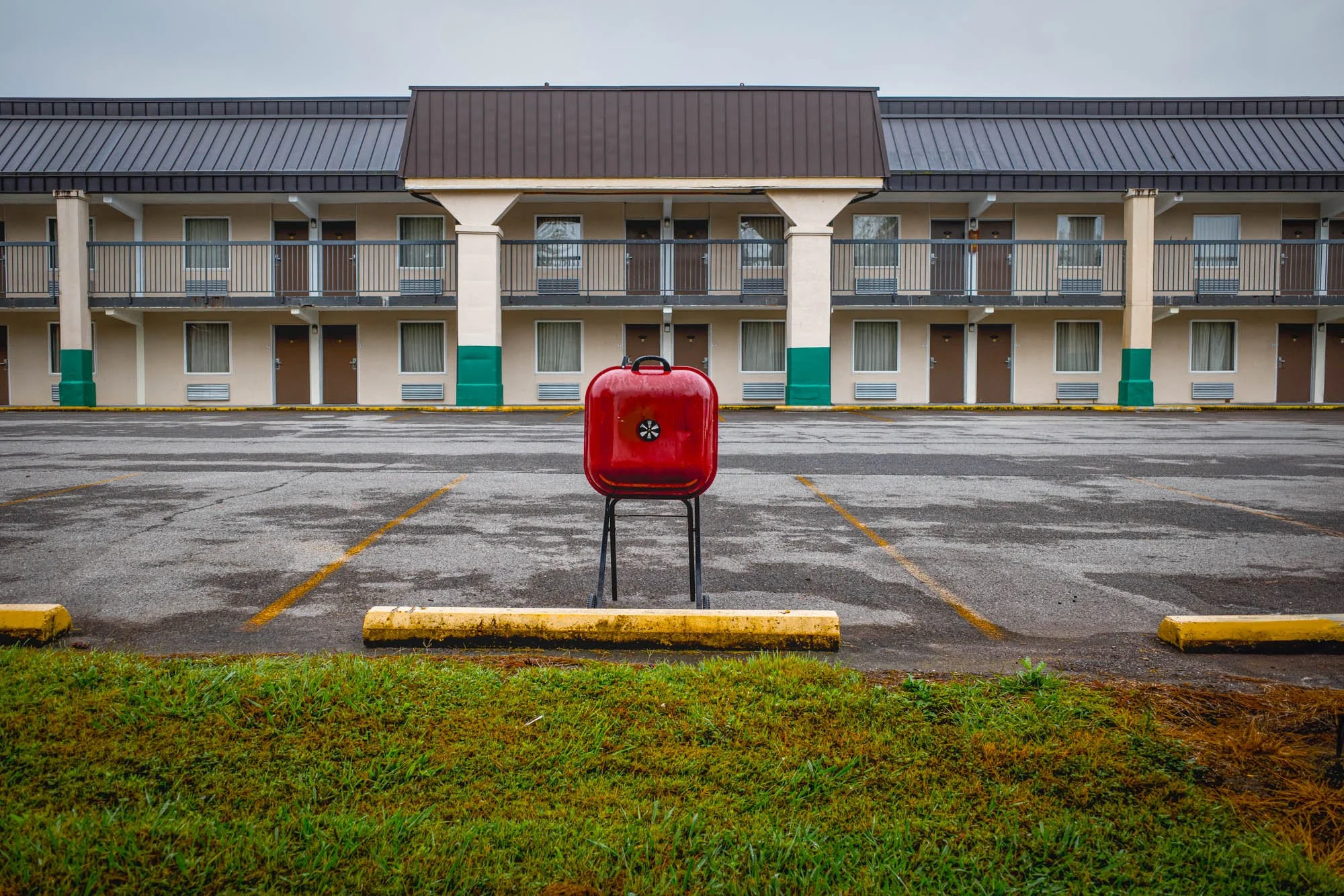 Empty parking lot with a red barbecue grill in the center, with a motel with three floors and balcony rooms in the background.