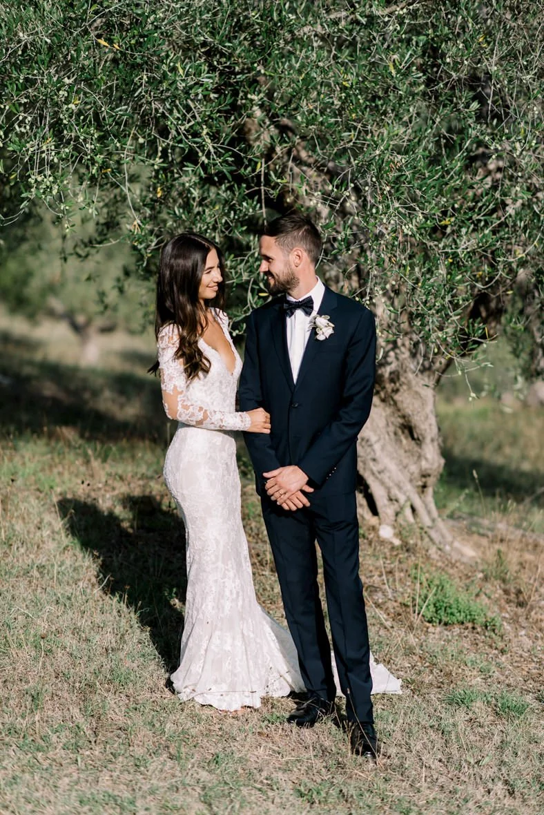 Wedding couple standing close together beside an olive tree at Conti di San Bonifacio in Tuscany.
