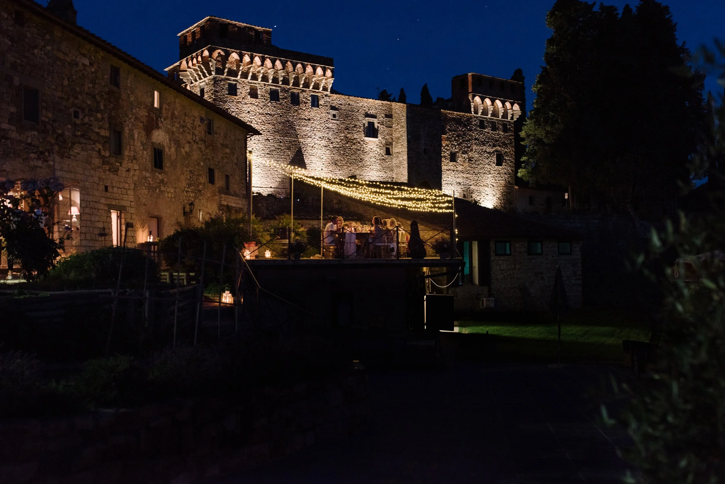 Evening wedding dinner at Castello del Trebbio illuminated by string lights against the castle walls.