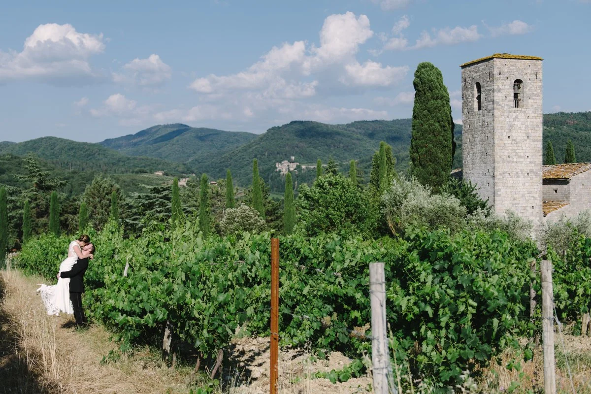 Couple kissing in the vineyard at Castello di Spaltenna with the castle tower visible in the background.