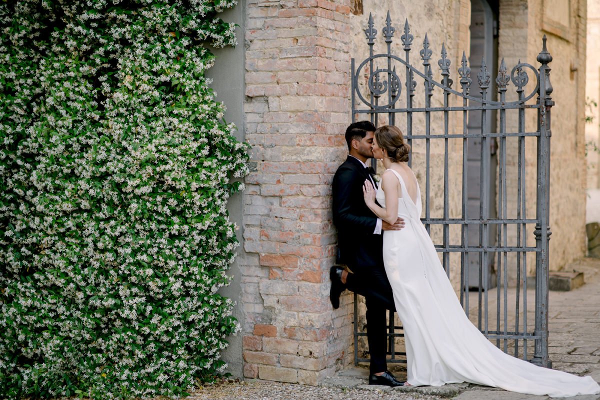 Bride and groom kissing at the entrance gate of Tenuta di Monaciano wedding venue.