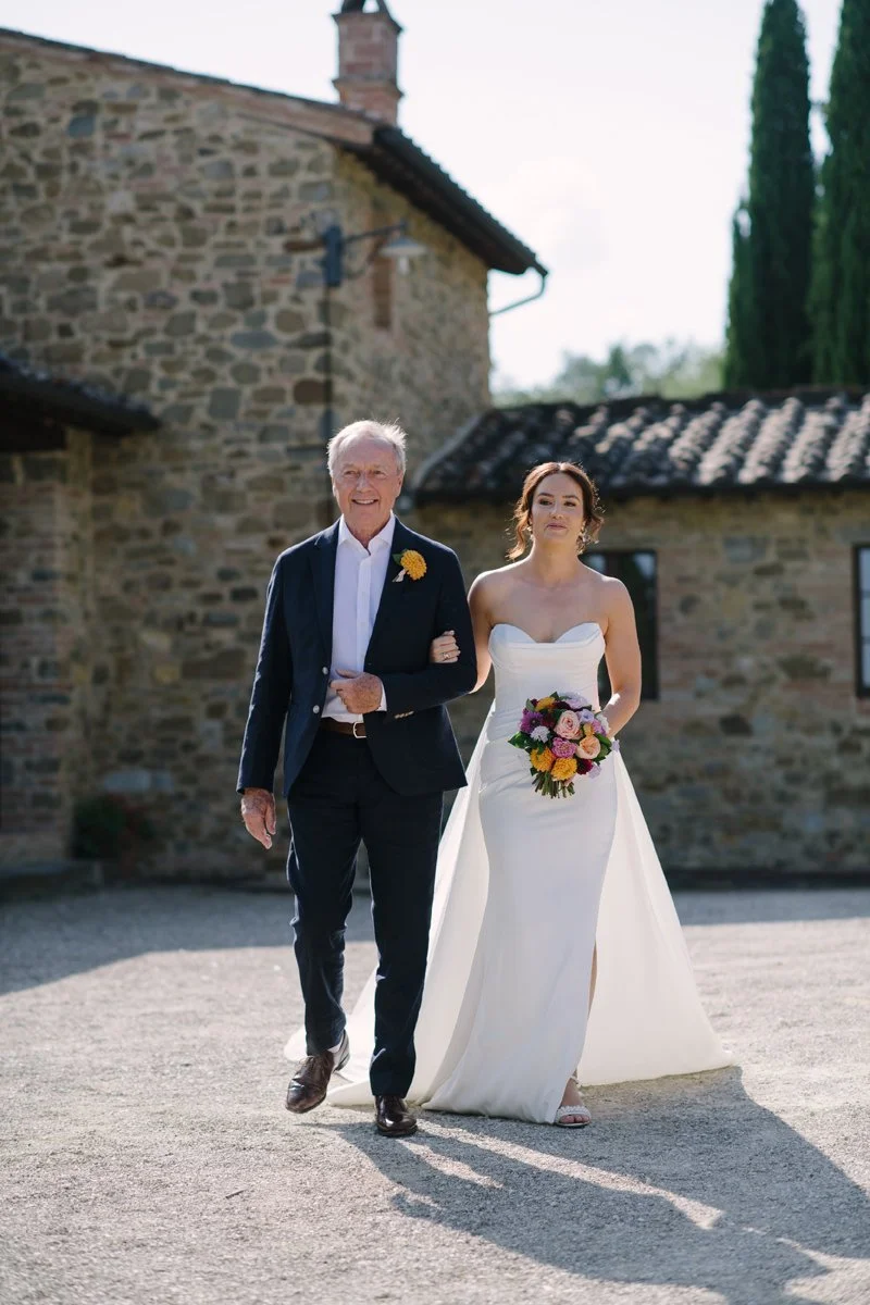 Bride walking with her father toward the ceremony at Casa Cornacchi, with the historic house in the background in Tuscany
