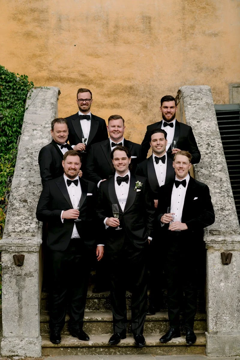 Groom and groomsmen standing on the villa stairs at Villa di Ulignano during the wedding, wearing tuxedos and sharing a relaxed moment.
