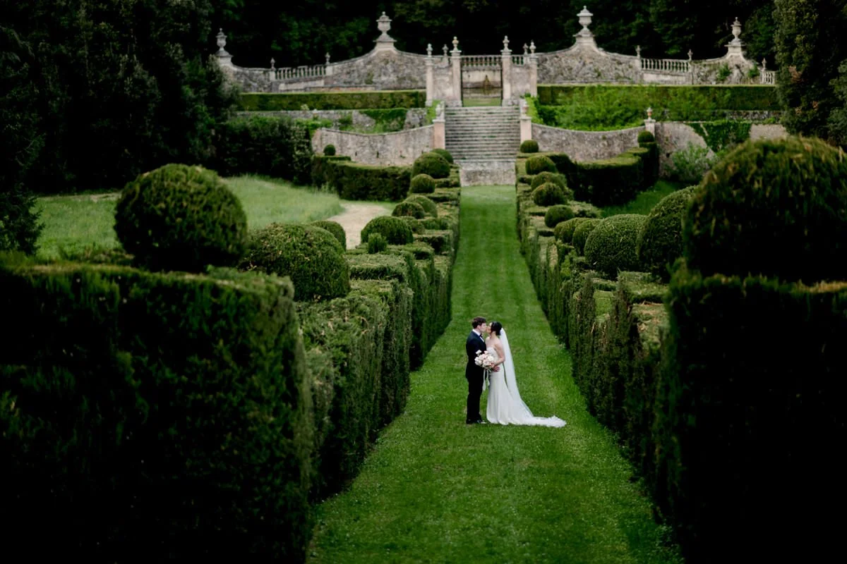 Couple kissing in the Italian garden at Castello di Celsa, surrounded by historic architecture and greenery.