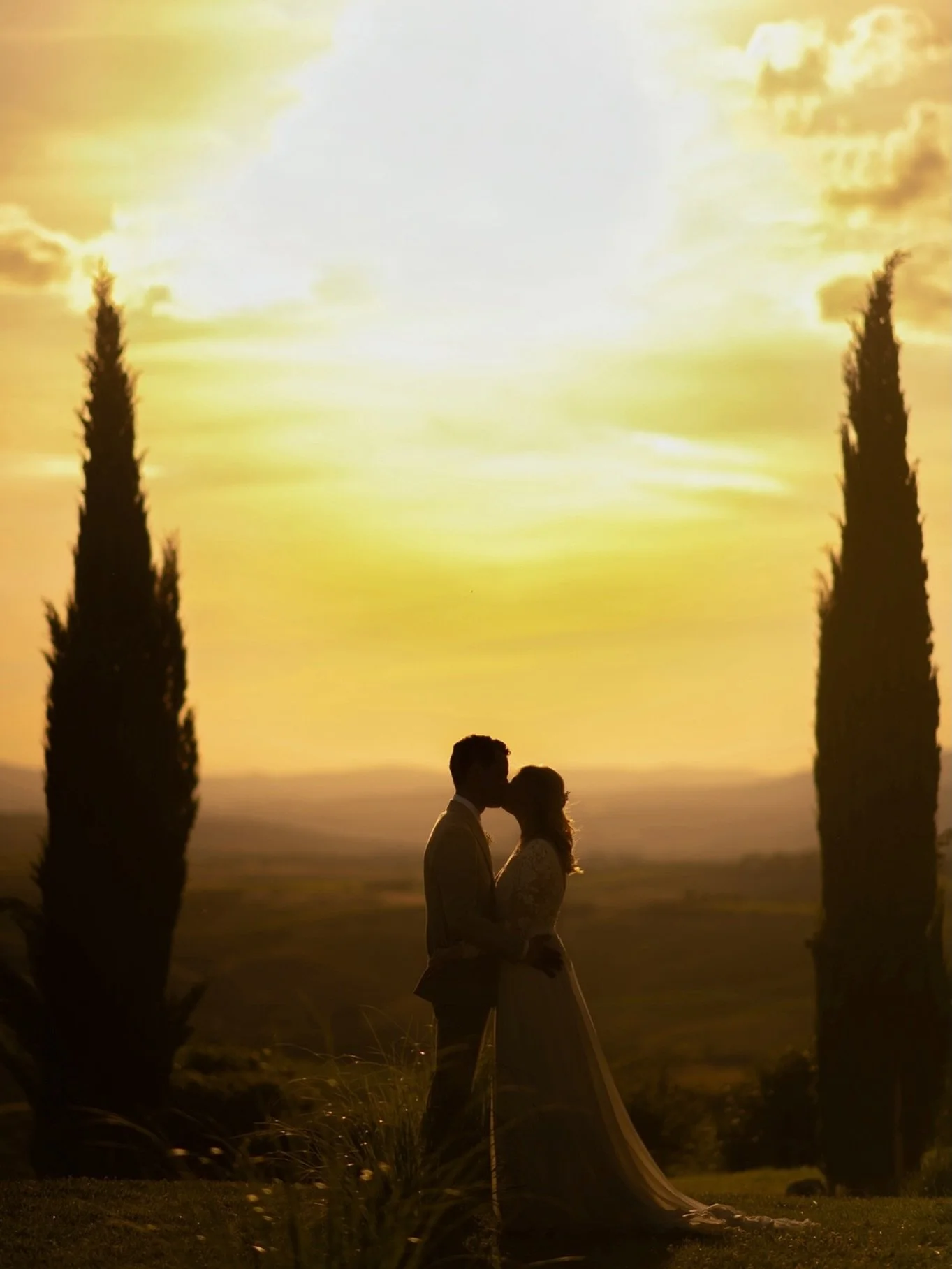 A sunset couple portrait at Capanna Suites near Montalcino, photographed between two tall cypress trees with the Tuscan hills falling into the background.

This is one of those quiet wedding photography moments where the landscape does half the work.