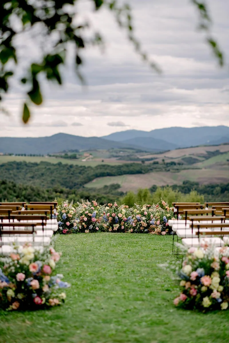 Wedding ceremony at Villa di Ulignano set beside the pool, using the main ceremony spot with open countryside views and colourful floral arrangements.