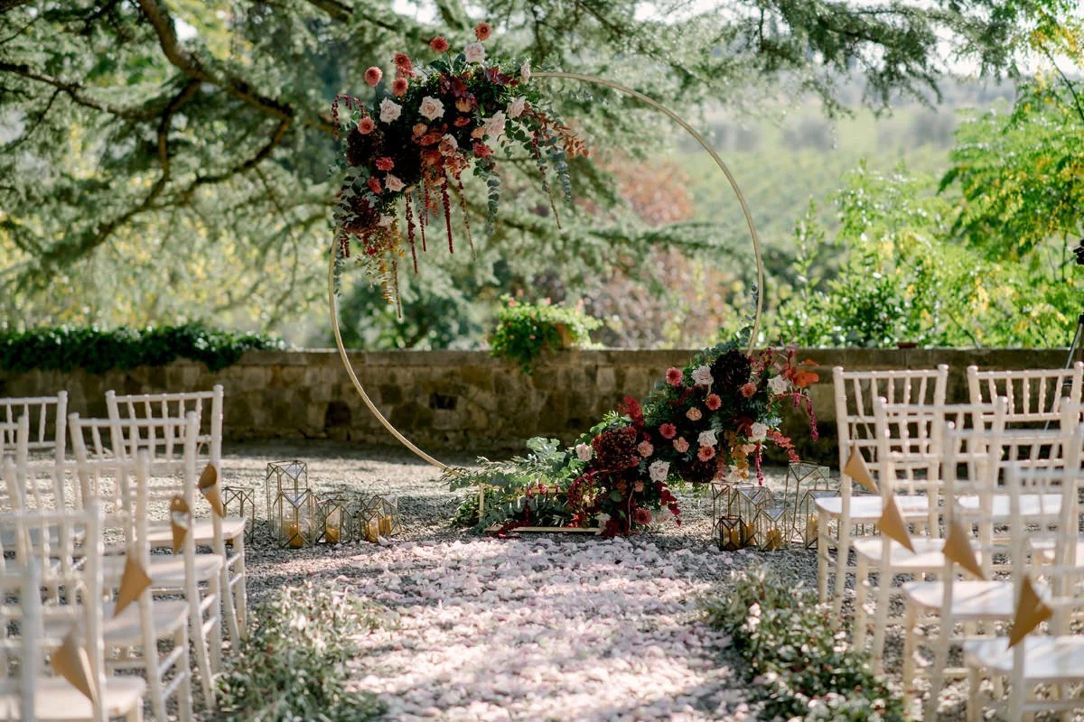 Outdoor wedding ceremony at Castello Il Palagio with floral decorations and a round arch in the castle gardens.