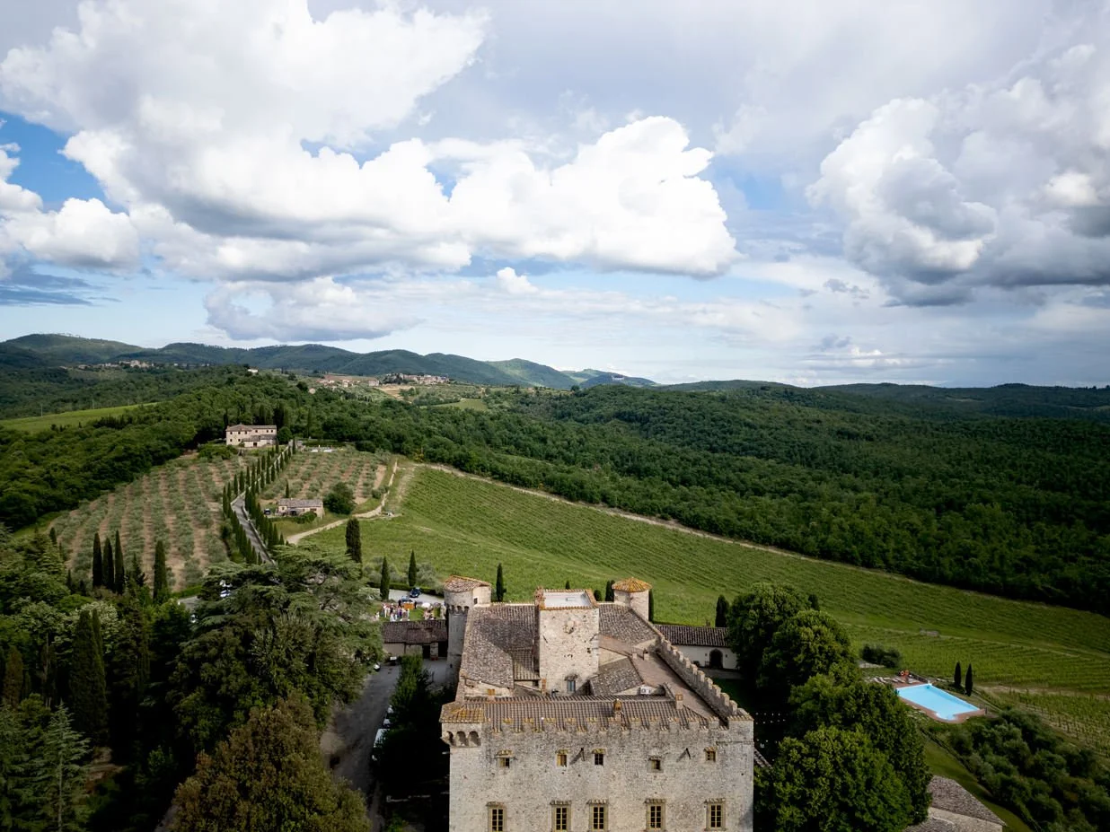 Aerial view of Castello di Meleto showing the castle surrounded by Chianti vineyards and rolling Tuscan hills.