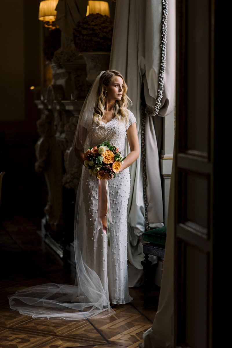 Bride standing by a window at Villa Cora, holding her bouquet and looking out toward the gardens.