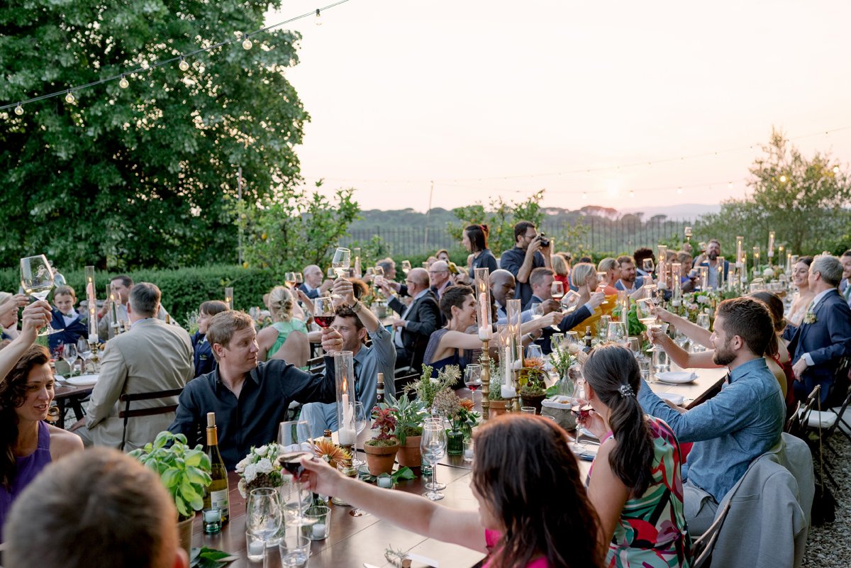 Wedding guests raising glasses and cheering during dinner at Castello di Bossi in Tuscany.