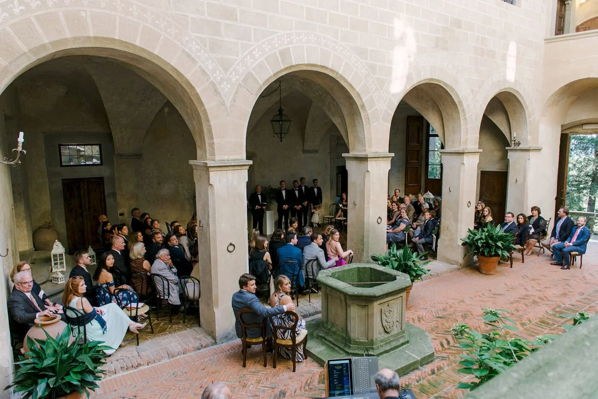 Wedding guests seated inside the covered stone courtyard at Castello di Montegufoni, waiting for the ceremony to begin.