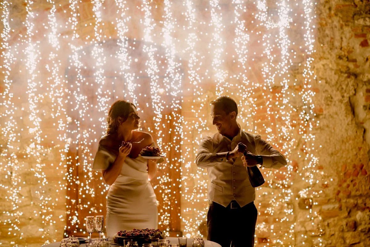 Bride and groom opening a bottle of prosecco while large sparklers light up the celebration at Villa Boscarello.
