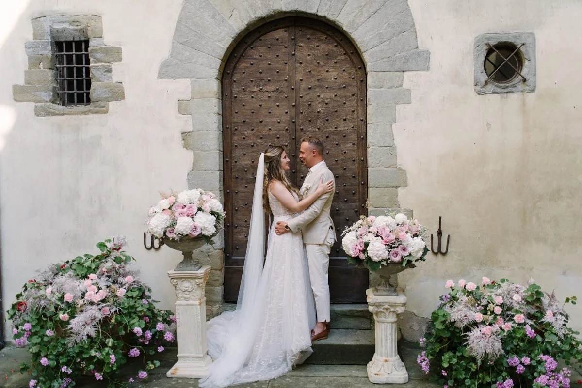 Bride and groom kissing in front of the large historic wooden door at Castello del Trebbio wedding venue.