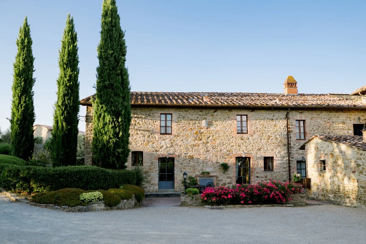 Main building of Casa Cornacchi framed by three tall Tuscan cypress trees in the countryside