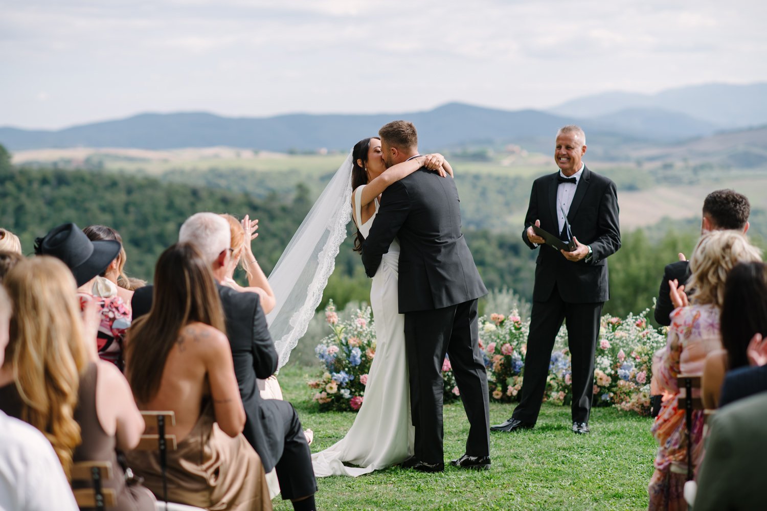 First kiss at Villa di Ulignano with the meadow floral wall and Volterra hills behind, October wedding by FunkyBird