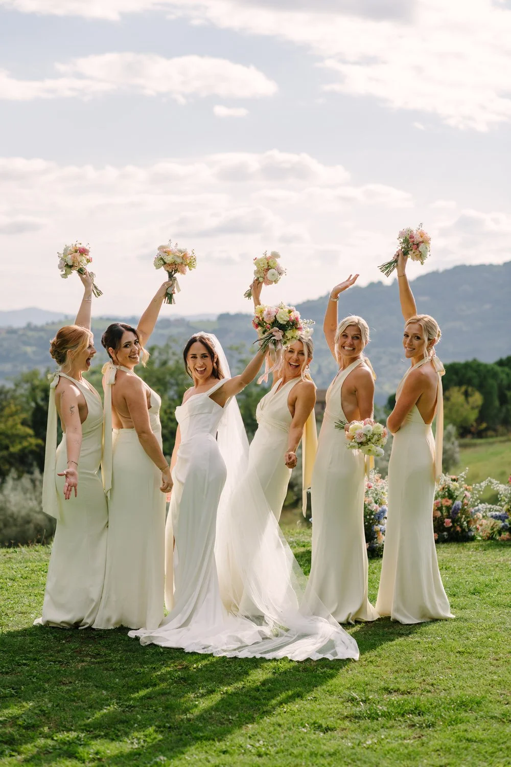 Bride and bridesmaids holding their bouquets up in the gardens of Villa di Ulignano, by FunkyBird