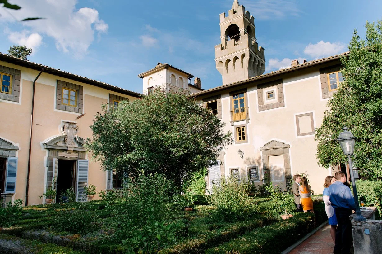 View of Castello di Montegufoni from the garden area during aperitivo, with guests gathering outdoors.