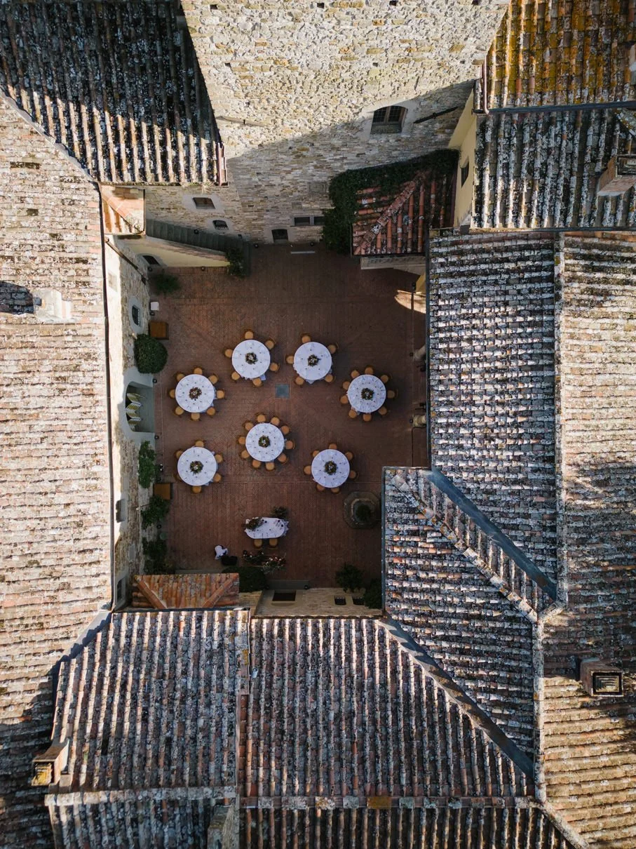 Drone view of the castle courtyard at Castello Il Palagio prepared with round tables for a wedding dinner.