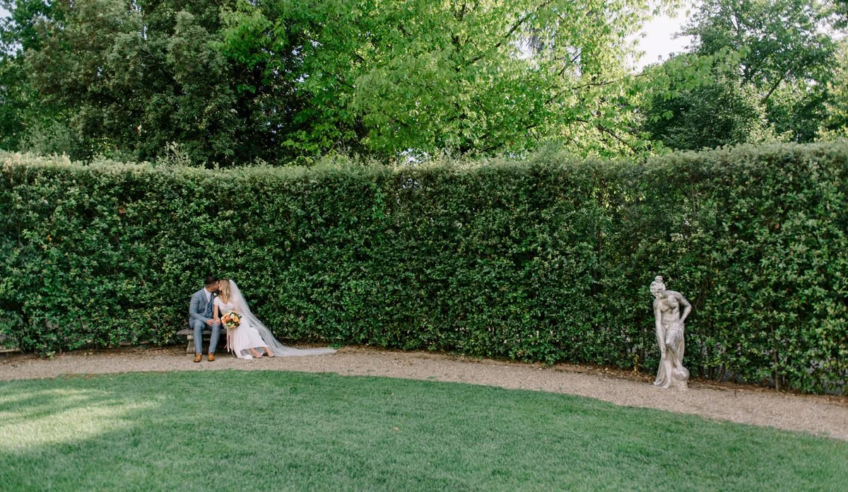 Wedding couple sitting together on a garden bench at Villa Cora, surrounded by greenery.