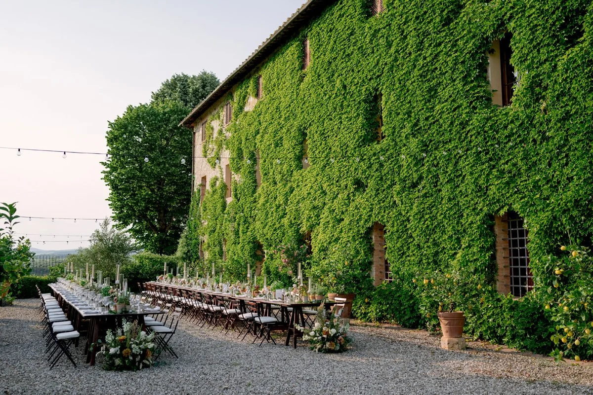 Wedding dinner setup with candles and floral decorations in front of the ivy-covered walls of Castello di Bossi in Tuscany.