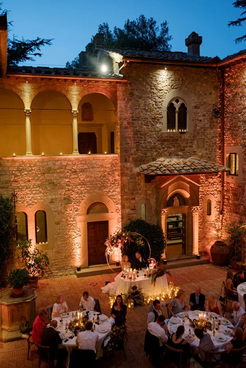 Night wedding dinner at Castello Il Palagio with the castle illuminated by spotlights during the celebration.