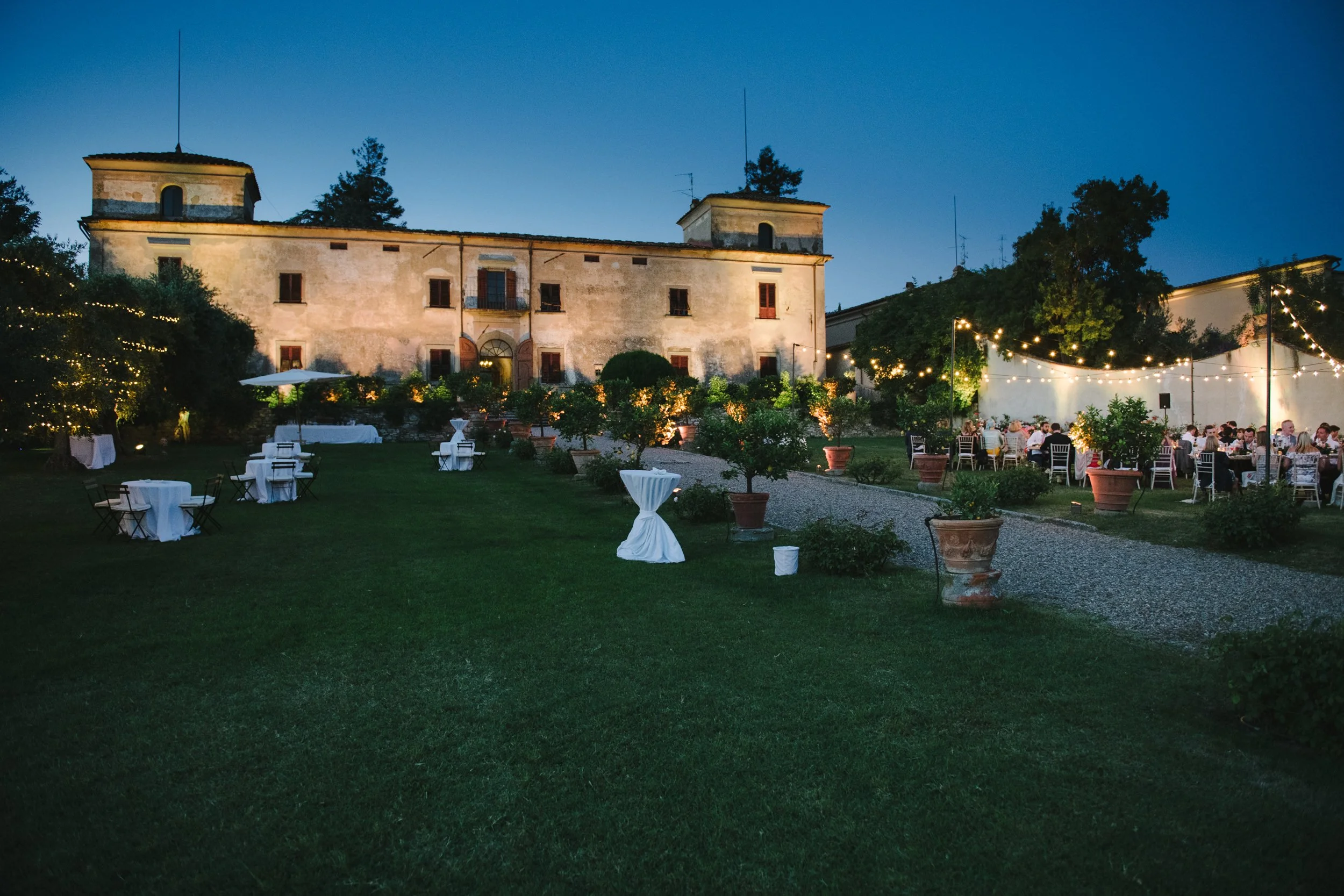 Wedding dinner at Villa Medicea di Lilliano at night with round tables and string lights in front of the villa