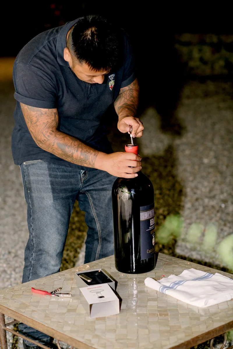 Castle staff opening a large bottle of wine produced from the Castello di Bossi vineyards during a wedding celebration.