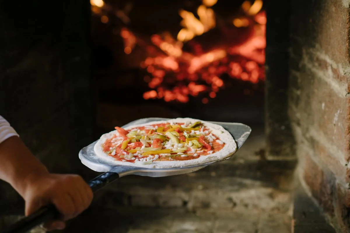 Pizza being placed into a wood-fired oven during the welcome dinner at Le Filigare wedding venue in Tuscany.