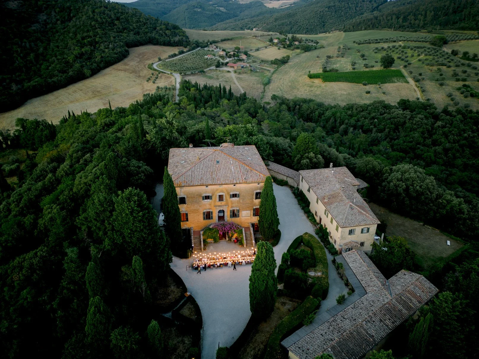 Outdoor dinner at Villa di Ulignano with string lights glowing above long tables on a warm Tuscan evening.