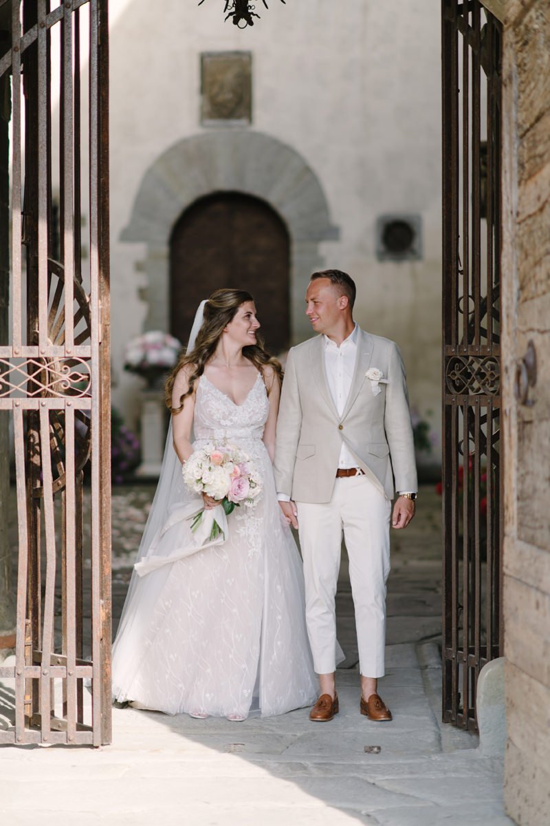 Couple standing at the stone entrance gate of Castello del Trebbio surrounded by Tuscan countryside.
