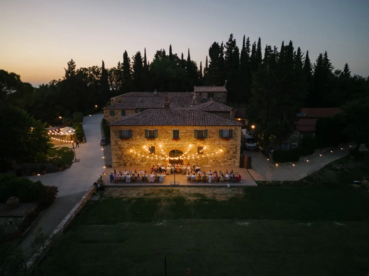 Drone view of a long wedding dinner table in front of the villa at Le Filigare at night with string lights.