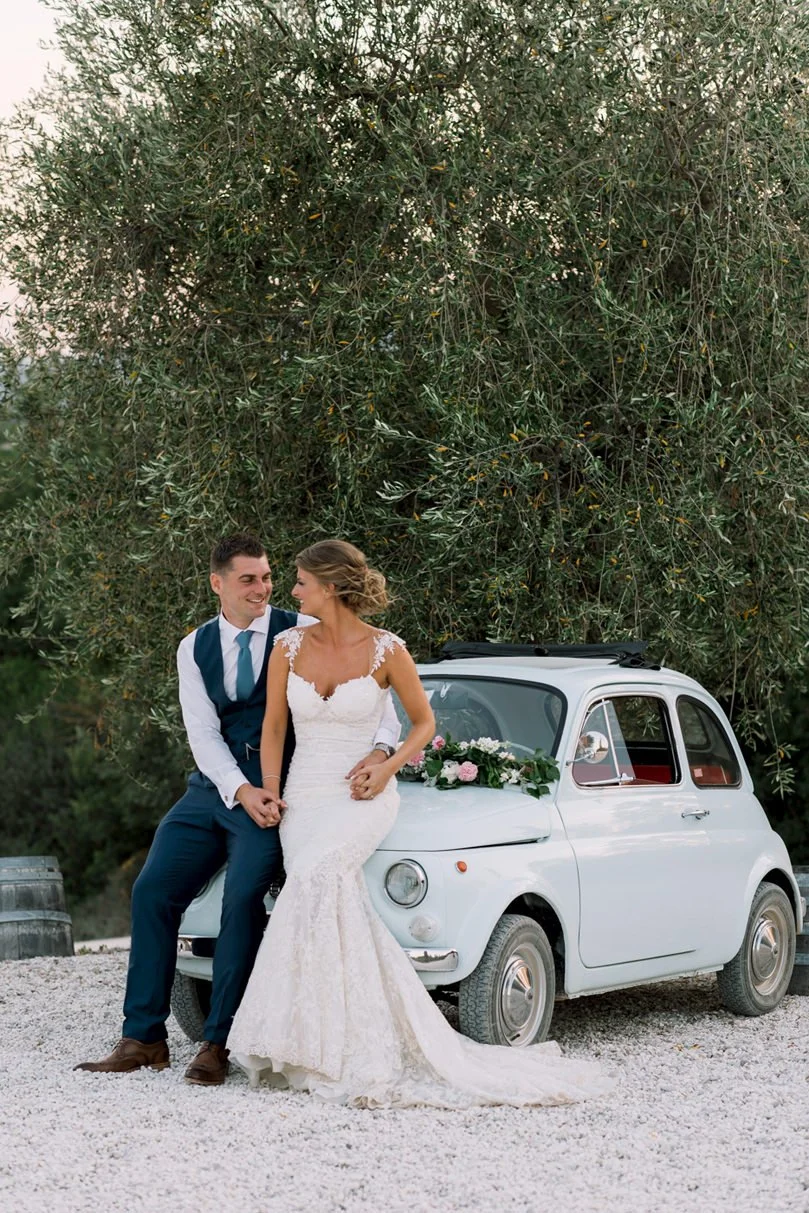 Wedding couple sitting closely on a Fiat 500 at Conti di San Bonifacio in Tuscany.