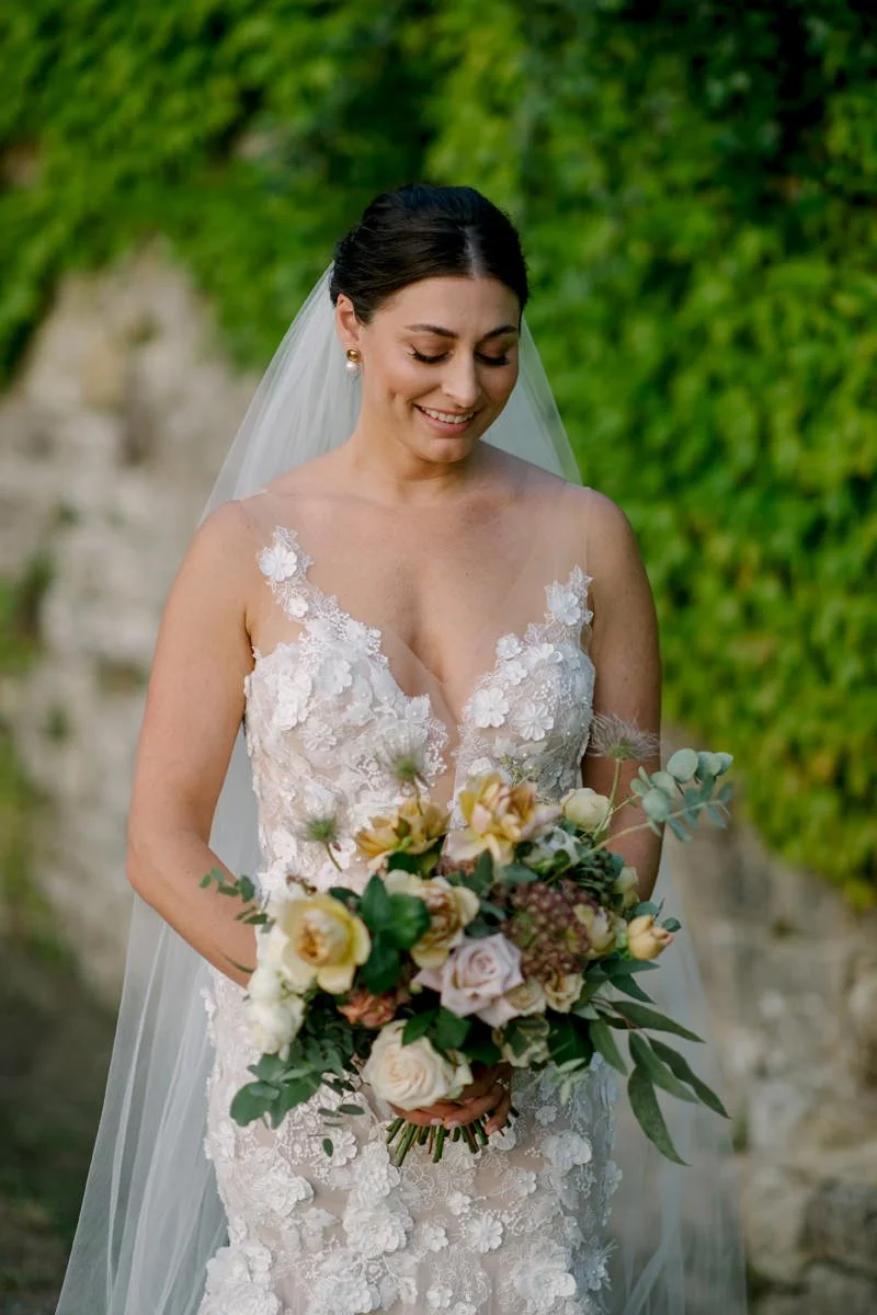 Bride holding her bridal bouquet in front of the historic castle at Castello di Bossi wedding venue in Tuscany.