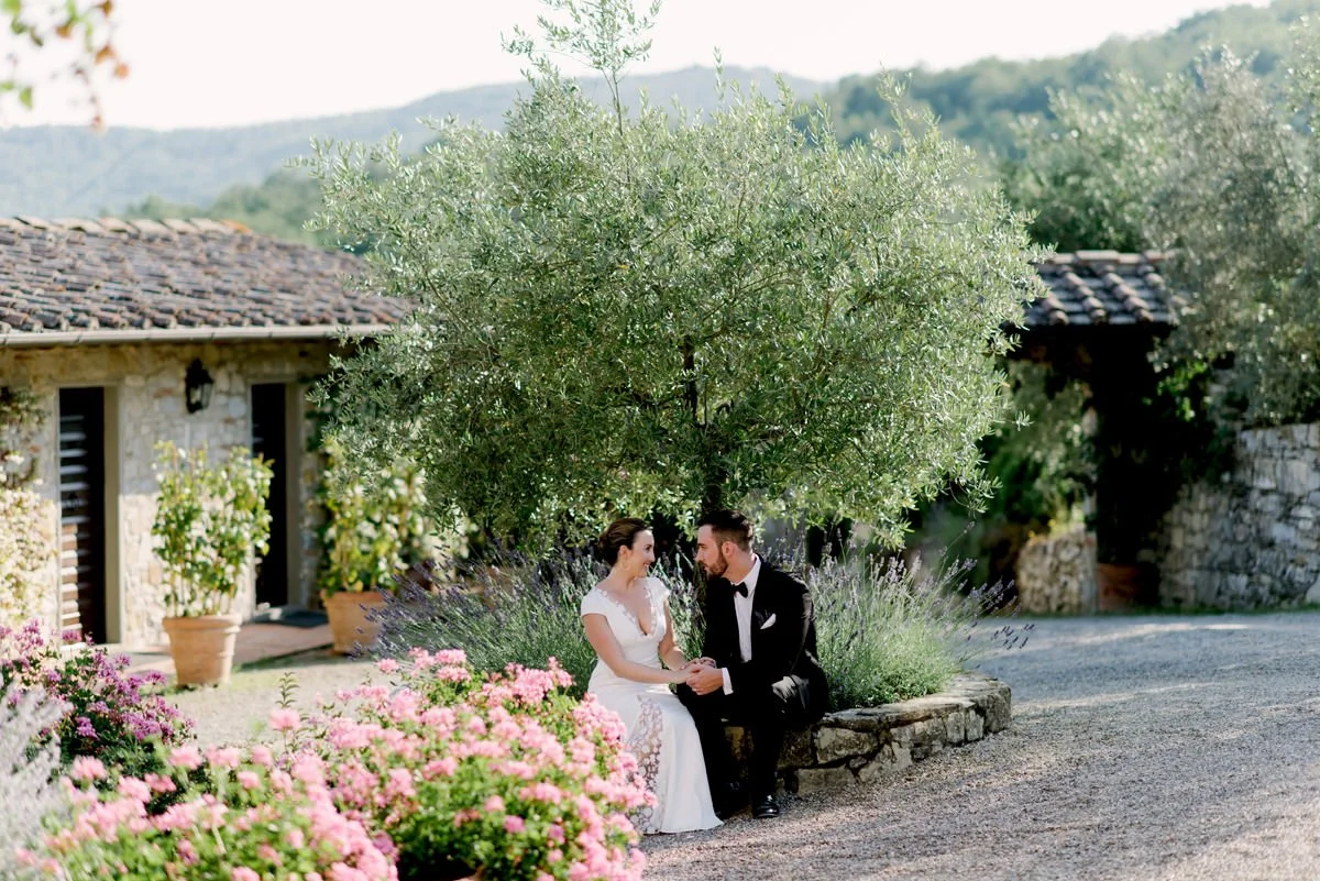 Wedding couple sitting closely on a stone wall next to an olive tree at Castello di Spaltenna.
