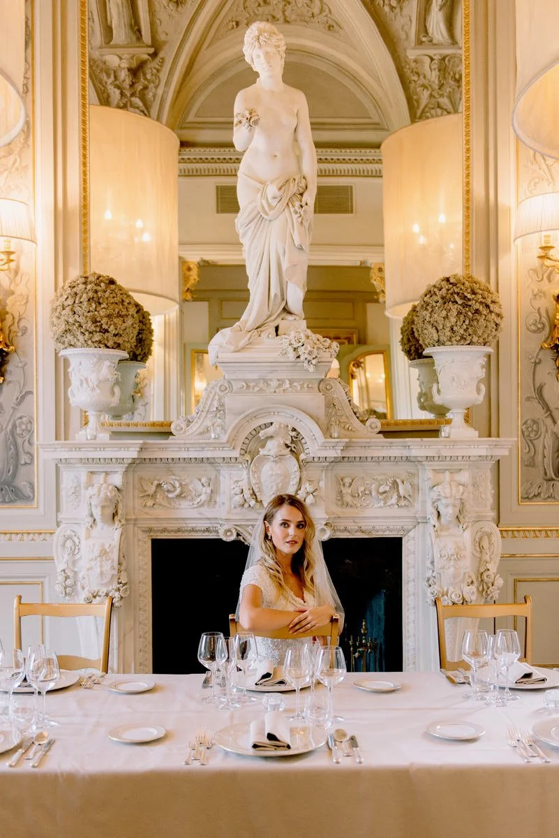 Bride seated at a table inside Villa Cora, framed by an ornate fireplace and classical statues.